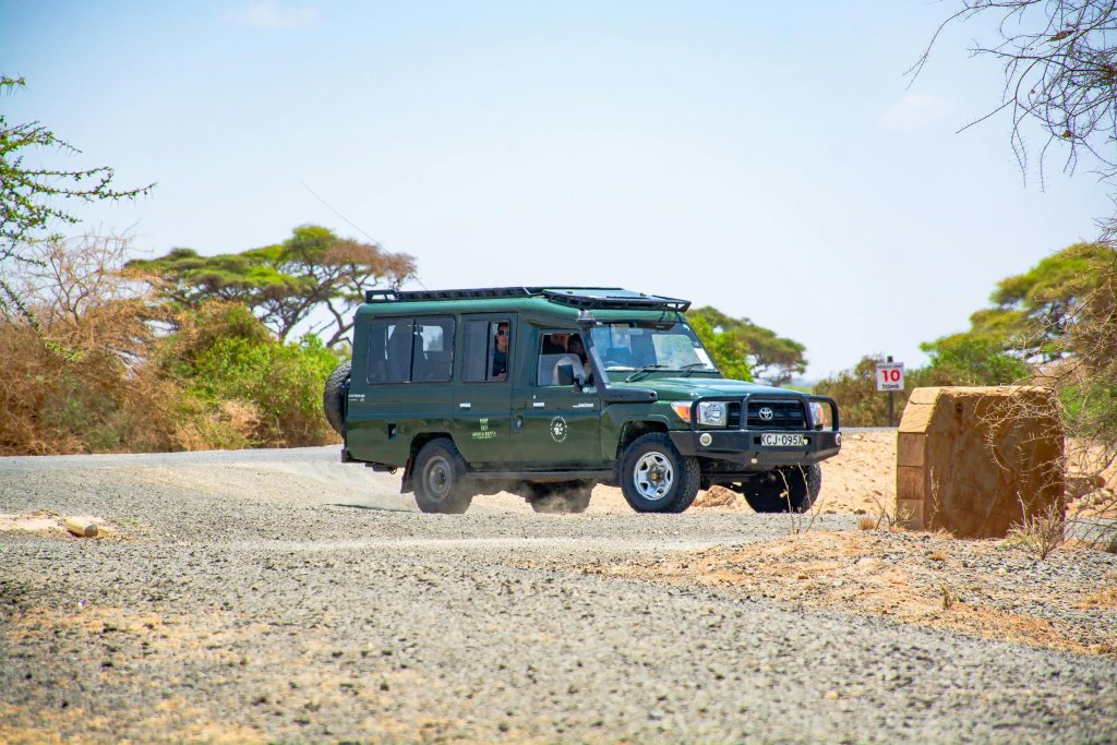 Green safari vehicle driving on rugged savannah road with scenic African landscape.